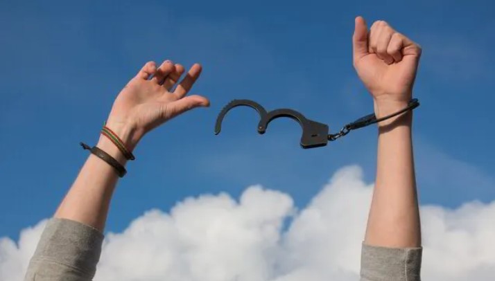 pexels-pixabay-247851-9540868 Person's hands held up in the sky breaking free from a set of handcuffs.