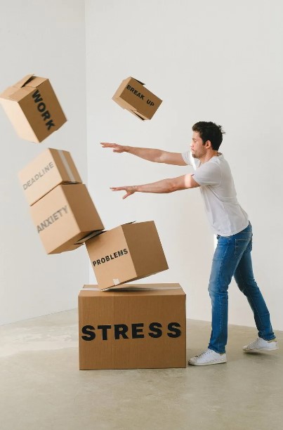 pexels-shvets-production-7203956-9797099 Man pushing over a pile of cardboard boxes marked with stress, anxiety and other words