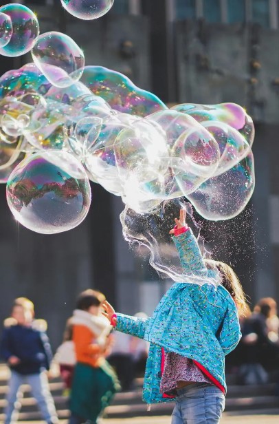 pexels-alexander-dummer-1919030-1002761 Little girl in a blue coat playing with large bubbles above her head.