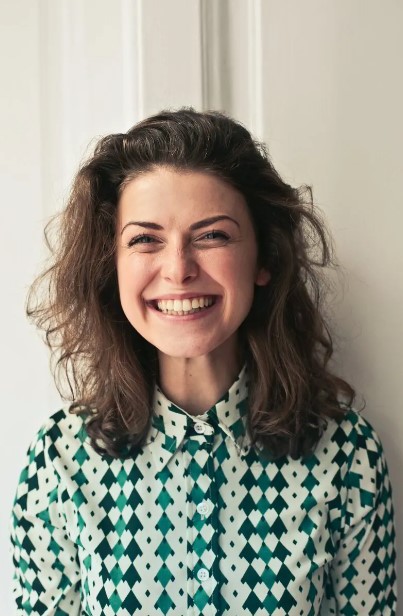 pexels-andrea-piacquadio-774909-1356074 Woman smiling in a green and white diamond patterned shirt with loose shoulder length brown curly hair.
